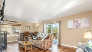 Un salon spacieux comprenant un canapé, une table basse et un téléviseur. Il y a un balcon avec vue sur les arbres.