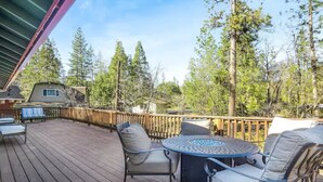 Une terrasse en bois, agréée de mobilier d’extérieur, notamment une table ronde et des chaises, le tout entouré de grands arbres.