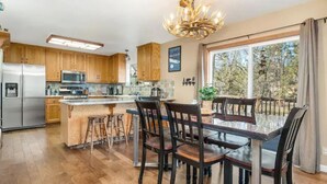 Une cuisine moderne avec des meubles en bois, un îlot central doté de tabourets et un coin repas avec une table et des chaises en verre.
