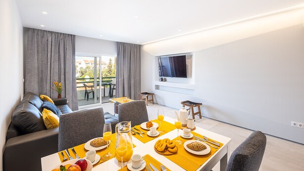 Quarto de hotel moderno com área de refeições, sofá e televisão presa na parede.