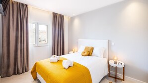 Quarto de hotel com cama, cortinas, mesa de cabeceira com abajur e uma janela.