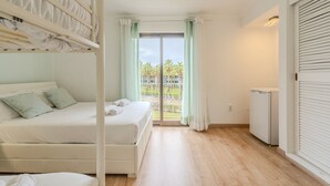 A bedroom with a bunk bed, a single bed, a view of a balcony with palm trees, and a white radiator. - #082 Families Only - São Rafael by Home Holidays (Albufeira)