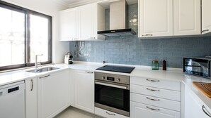 A modern kitchen with white cabinets, a stainless steel oven, a black induction cooktop, and a blue-tiled backsplash. - #082 Families Only - São Rafael by Home Holidays (Albufeira)