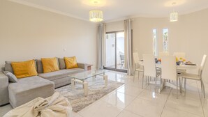A modern living room with a sofa, glass coffee table, dining table with chairs, and a large sliding glass door leading to an outdoor area. - #082 Families Only - São Rafael by Home Holidays (Albufeira)