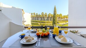 A breakfast table with plates, cutlery, and fruit on a balcony overlooking a landscaped garden. - #082 Families Only - São Rafael by Home Holidays (Albufeira)