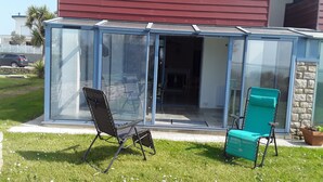 A glass-enclosed patio with two chairs, a stone wall, and a view of the house's interior. - Bright, sea-view apartment with direct beach access (Roscoff)