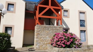 A modern building with a stone base and a red wooden structure on top, surrounded by pink flowers. - Bright, sea-view apartment with direct beach access (Roscoff)