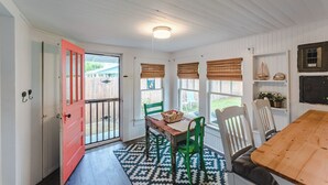 Un comedor acogedor con una mesa y sillas de madera, un tapete estampado y vistas al patio trasero a través de ventanas grandes con persianas.