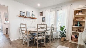 Un comedor con una mesa y sillas de madera, una planta en maceta y una estantería con diversos objetos.
