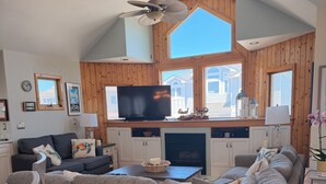 A living room with a sectional sofa, a flat-screen TV, a fireplace, and wooden paneled walls. - Semi Oceanfront 5 bedroom dog friendly cottage 10 feet to beach access (Corolla)