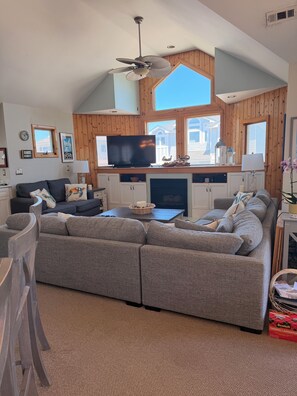 A living room with a sectional sofa, a flat-screen TV, a fireplace, and wooden paneled walls.