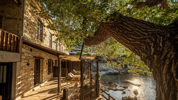 Un bâtiment en pierre doté d’un balcon donnant sur une rivière, avec des places assises en plein air et une vue sur l’eau.