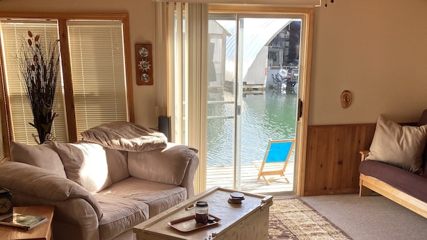 Een gezellige woonkamer met een bank, een bijzettafeltje en uitzicht op een boot door een schuifpui.