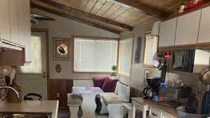 Een kleine keuken met witte kasten, een fornuis en een eethoek met een tafel en stoelen.