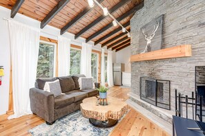 A modern living room with a stone fireplace, wooden beams, and a grey sofa.