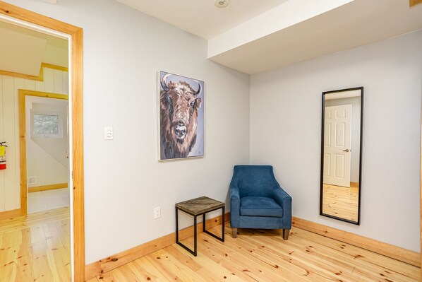 A room with a wooden floor, a blue armchair, a small table, and a painting on the wall.