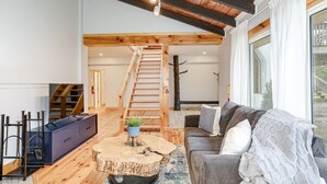 En rummelig stue med en trætrappe, en sofa, et sofabord og et fjernsyn.