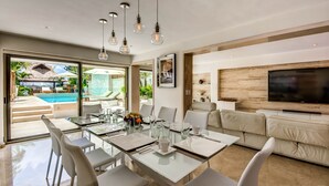 Ein modernes Wohnzimmer mit einem Glastisch, weißen Stühlen, einem beigen Sofa und einem flachbildfernseher an der Wand.