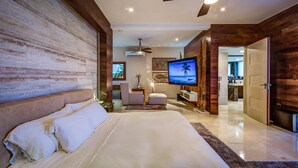 Ein modernes Schlafzimmer mit einem großen Bett, einem Deckenventilator, einem Fernseher und einer Wand mit Holzpaneelen.
