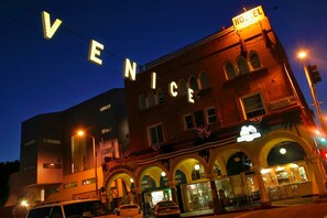 Ein Gebäude, an dem ein Schild mit leuchtenden Schriftzügen „HOSTEL“ und „VENICE“ angebracht ist.