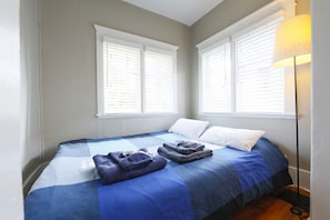 Ein Schlafzimmer mit einem Bett, zwei Fenstern mit Jalousien und einer Lampe.