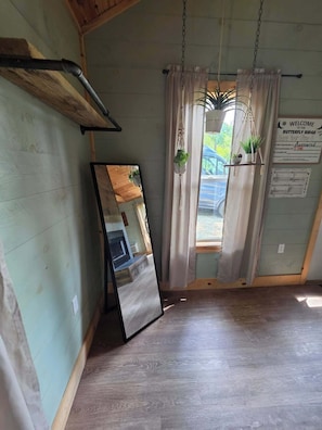 A room with a wooden floor, a large mirror, and a window with curtains. - Butterfly Ridge at Avenwood Cabins (New Straitsville)