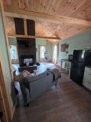 A cozy living area with a fireplace, sofa, and kitchen area with a refrigerator.