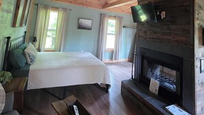 A spacious room with a bed, a fireplace, a television, and a ceiling fan. - Butterfly Ridge at Avenwood Cabins (New Straitsville)