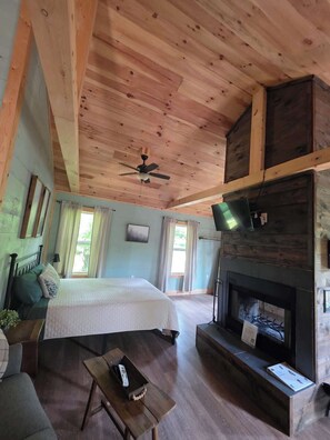 A spacious room with a bed, a fireplace, a television, and a ceiling fan. - Butterfly Ridge at Avenwood Cabins (New Straitsville)