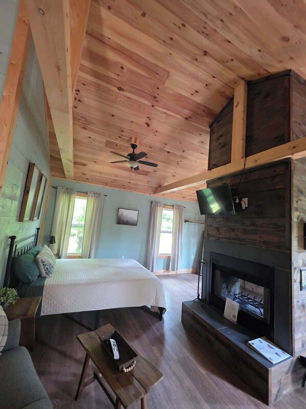 A spacious room with a bed, a fireplace, a television, and a ceiling fan.
