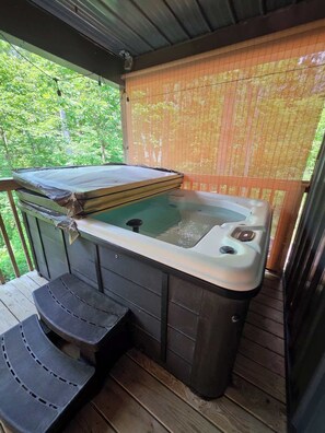 A hot tub with a wooden deck, a step for access, and a bamboo screen. - Butterfly Ridge at Avenwood Cabins (New Straitsville)