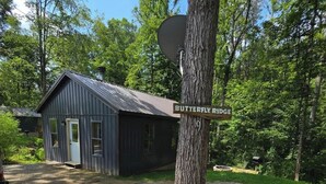 A rustic cabin labeled 'Butterfly Ridge' with a gravel driveway and surrounding trees. - Butterfly Ridge at Avenwood Cabins (New Straitsville)