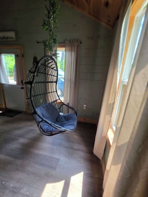 A room with a hanging chair, a potted plant, a door, and a window. - Butterfly Ridge at Avenwood Cabins (New Straitsville)