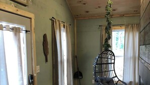 A room with a hanging chair, a door with curtains, a wall-mounted coat rack, and a window with a view of greenery. - Butterfly Ridge at Avenwood Cabins (New Straitsville)