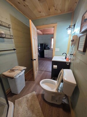 A compact bathroom with a toilet, sink, and a small trash bin. - Butterfly Ridge at Avenwood Cabins (New Straitsville)