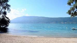 A beach with clear water, a distant mountain, and a bench.