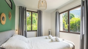 A bedroom with a bed, curtains, a window, and a view of greenery.