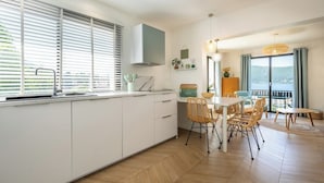 A modern kitchen with white cabinets, a dining area with wicker chairs, and a view of the sea.