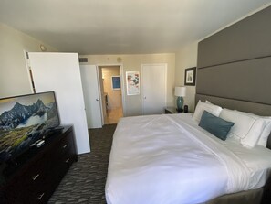 Une chambre d’hôtel avec un grand lit, une commode, une télévision et une porte donnant sur un couloir.