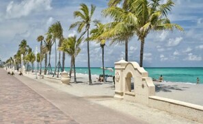 A beach with a paved walkway lined with palm trees and a clear view of the ocean.