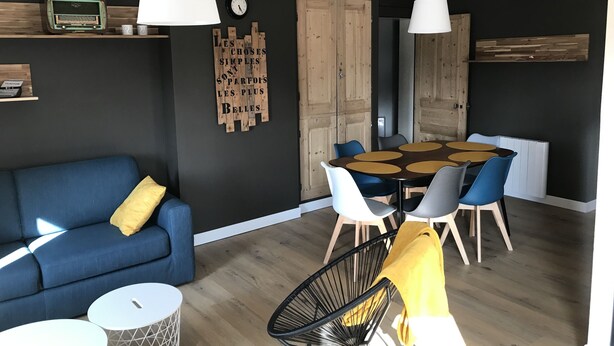 Een moderne woonkamer met een blauwe bank, een ronde eettafel met blauw-witte stoelen en een houten kast.