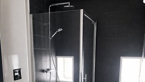 Een moderne badkamer met een douchecabine van glas, een wit toilet, een wasmachine en een wastafel.
