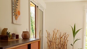 Ett rum med ett träskåp, ett konstverk som hänger på väggen, ett fönster med utsikt över grönområden och en blomsteruppsättning.