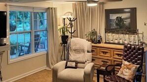 A living room with a beige armchair, a brown leather chair, a fireplace, a TV, and a window with curtains.