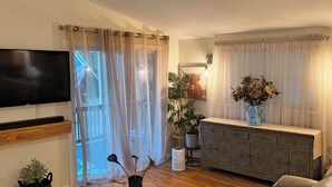 A living room with a TV, a sofa, a coffee table, a cabinet, and a plant.