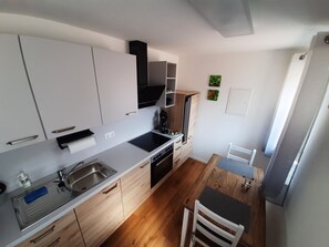 A compact kitchen with white cabinets, a black stove, and a wooden dining table. - Guesthouse Buberl, near Legoland and Skylinepark (Krumbach (Schwaben))
