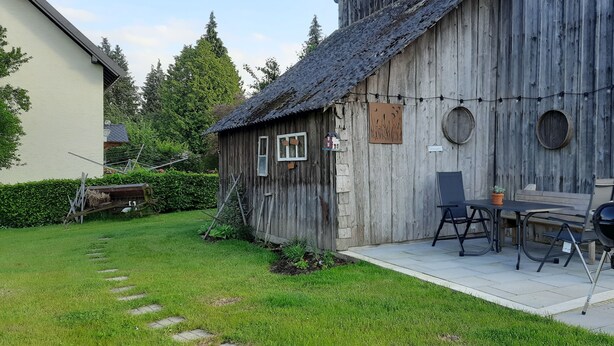Un bâtiment rustique en bois doté d’un patio comprenant une table et des chaises, un barbecue et une guirlande lumineuse.
