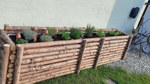 Un bac à fleurs en bois, contenant diff érentes plantes, placé contre un mur.