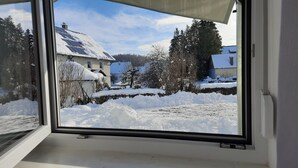 Une vue par la fenêtre sur un paysage enneigé, avec des maisons et des arbres.