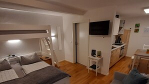 Une pièce compacte comprenant un lit superposé, un canapé, une petite table, un téléviseur et un coin cuisine.